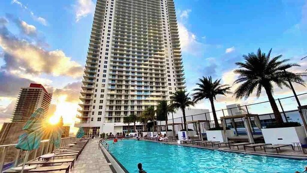 A high-rise hotel with a swimming pool, palm trees, and a sunset. - Stylish Luxury Apartment with Unforgettable Views (Hollywood)