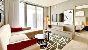 A modern hotel room with a sofa, a small round table, a TV mounted on the wall, and a large window with a view of buildings. - Stylish Luxury Apartment with Unforgettable Views (Hollywood)