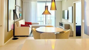 Ein modernes Hotelzimmer mit Essbereich, einer Sitzecke, einem Fernseher und einem großen Fenster.
