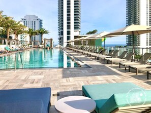 Un espace piscine d’hôtel avec des chaises longues, une piscine et de grands immeubles en arrière-plan.