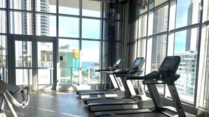 Une salle de sport équipée de tapis de course, dotée de grandes fenêtres et offrant une vue sur de hauts immeubles.