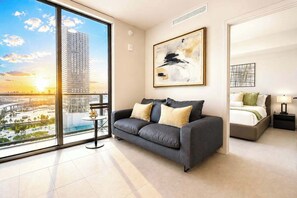 A modern living room with a sofa, a small table, a bed, and artwork on the walls. - Luxury Bayview 1BR in Downtown Near Kaseya (Miami)