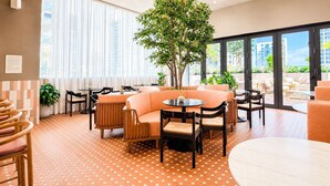 Una hall d'albergo con area salotto, un albero grande e vista sull'esterno.