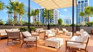 Una terrazza lounge con posti a sedere all'aperto, un pavimento decorato e moderni edifici sullo sfondo.