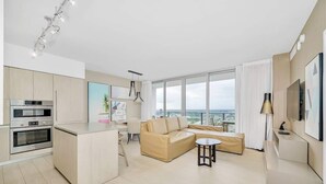 A modern kitchen with built-in appliances, a dining area with a sofa, and a large window offering a view. - 1 BR Sunset views Hollywood Beach (Hollywood)