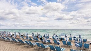 A beach with rows of blue lounge chairs and striped umbrellas, a clear sky, and calm sea. - 1 BR Sunset views Hollywood Beach (Hollywood)
