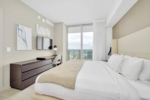 A modern hotel room with a large bed, a desk, and a view of the city. - 1 BR Sunset views Hollywood Beach (Hollywood)