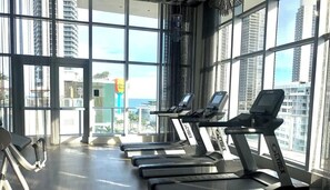 A gym with treadmills and exercise equipment, large windows, and a view of tall buildings. - 1 BR Sunset views Hollywood Beach (Hollywood)