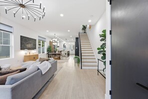 A modern interior with a sofa, dining area, staircase, and a kitchen in the background. - Linwood House | Rooftop, Hot Tub, Sleeps 15 | (Columbus)
