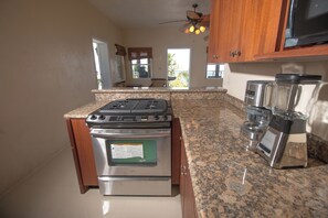A kitchen with a stainless steel stove, granite countertop, wooden cabinets, and a ceiling fan. - Charming 1-bedroom villa atop Bordeaux Mountain (Coral Bay)