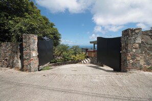 A gated entrance with stone walls and a view of the ocean. - Charming 1-bedroom villa atop Bordeaux Mountain (Coral Bay)