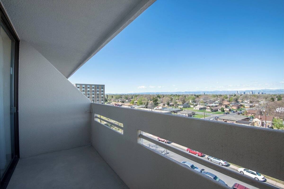 Un balcon offrant une vue dégagée sur un quartier résidentiel, un parking et des montagnes lointaines.