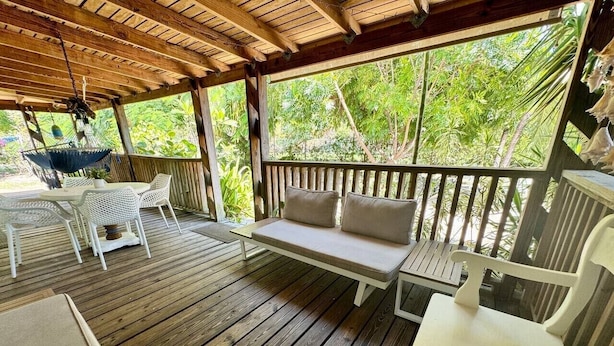 Eine Holzterrasse mit einer Hängematte, weißen Korbstühlen und einer gepolsterten Bank.