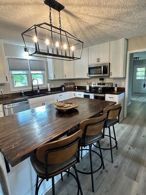 A modern kitchen with a central island, white cabinetry, a stainless steel oven, and a hanging light fixture.