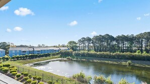 A residential area with a pond, blue houses, and a forest in the background. - Surfside Beach Retreat - Pool Access - 4BR - 1 Mile to Beach (Myrtle Beach)
