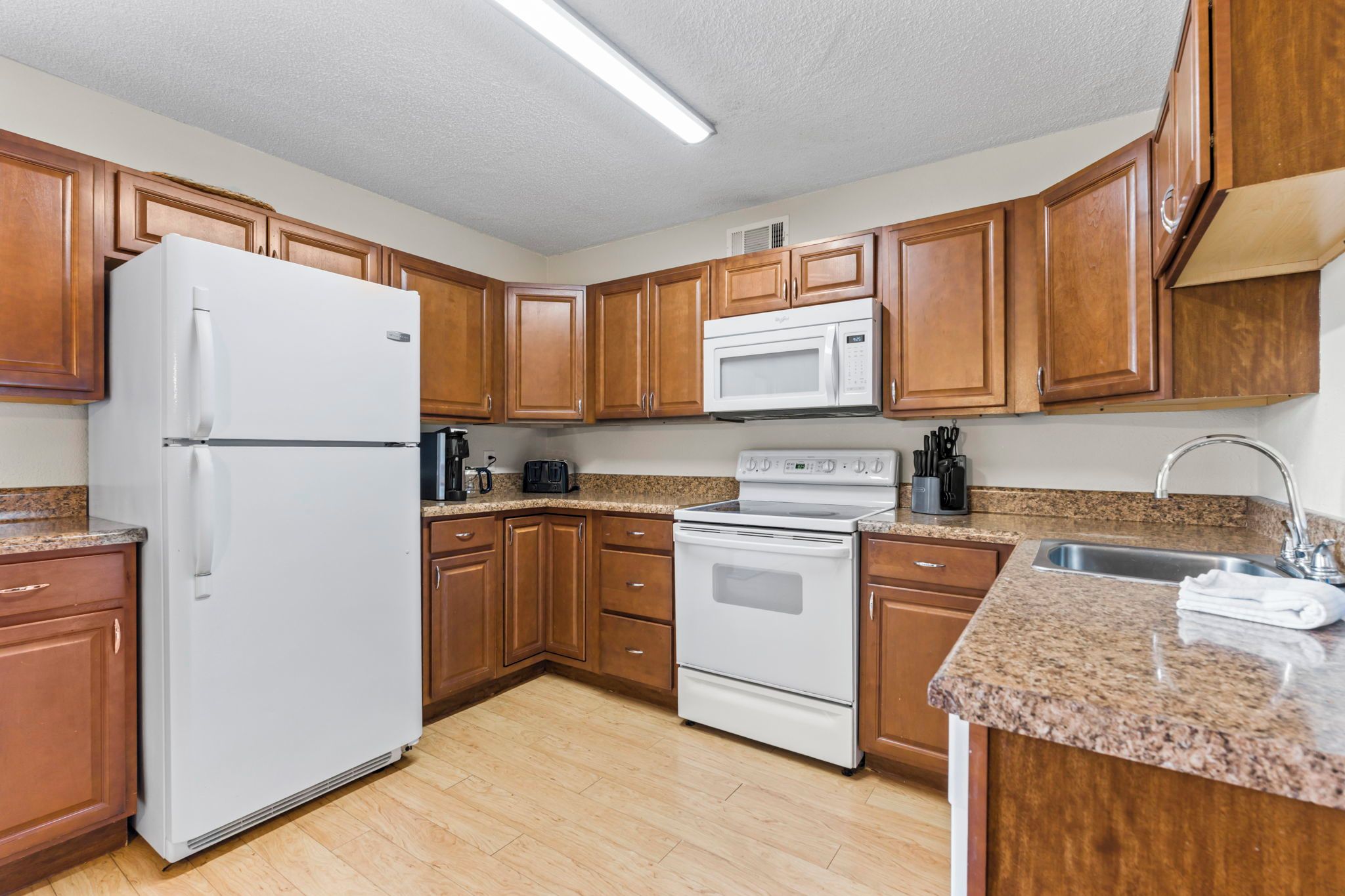 A kitchen with wooden cabinets, a white refrigerator, a microwave, an oven, and a granite countertop.