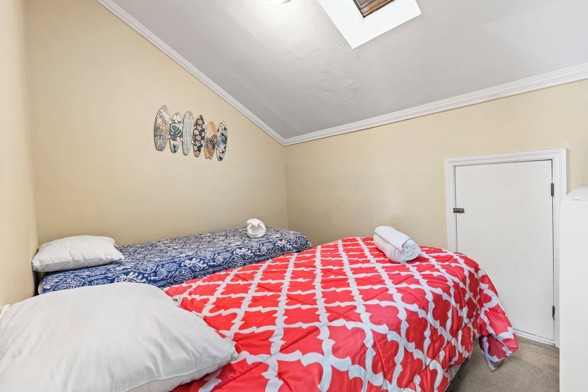 A bedroom with two beds, a white door, and a skylight.