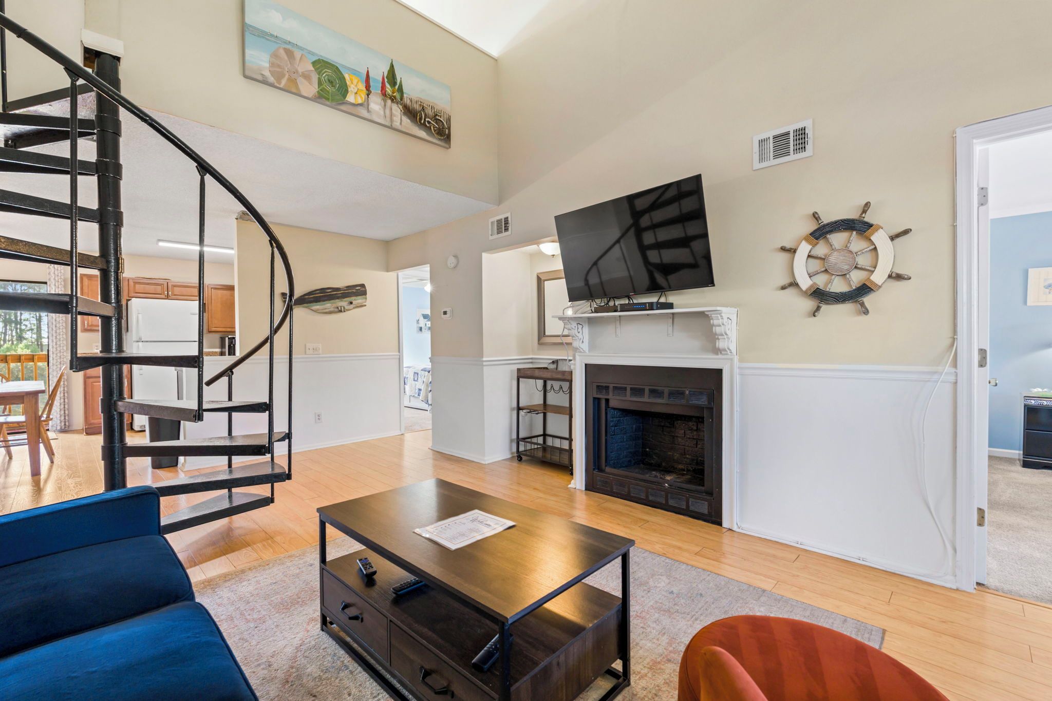 A living room with a fireplace, a TV mounted above it, a staircase, and a dining area in the background.