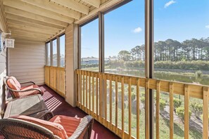 Eine überdachte Veranda mit Korbstühlen, einem Holzbalkon und Blick auf einen See und Bäume.