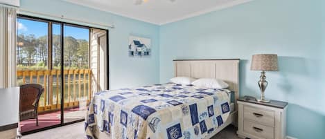 A bedroom with a bed, a nightstand, a lamp, a ceiling fan, a window, and a door leading to a balcony.