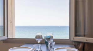 Ein Tisch mit zwei Weingläsern, einem Wasserglas, einem Teller und einem Fenster mit Blick auf das Meer und Boote.