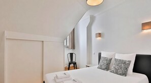 Ein modernes Hotelzimmer mit Bett, Sessel, Nachttisch und einer Wandleuchte.