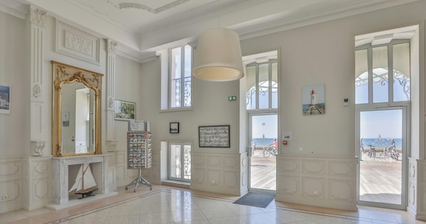 Eine geräumige Lobby mit einem großen Spiegel, einem Kamin, einer Präsentationswand und großen Fenstern mit Blick auf das Meer.