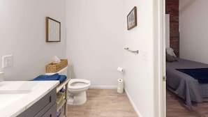 A bathroom with a toilet, a sink, and a basket of toiletries.