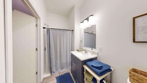A bathroom with a shower curtain, a sink, a mirror, and towels.