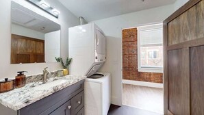 A bathroom with a white sink, a mirror, a white washing machine, and a wooden door.