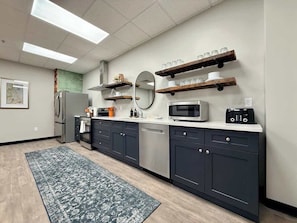 A modern kitchen with dark cabinets, stainless steel appliances, and wooden shelves.