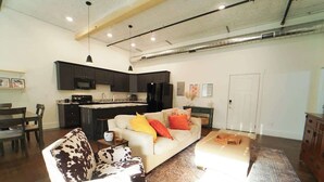 Ein modernes Wohnzimmer mit Sofa, Couchtisch und Küchenbereich mit dunklen Schränken und Geräten.