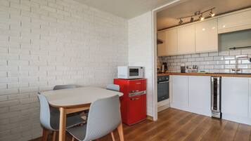 Una cocina compacta con paredes de ladrillo blanco, un electrodoméstico rojo y una zona de comedor con mesa y sillas.