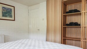 Un dormitorio con pared de ladrillo blanco, una puerta blanca, una cama con colcha estampada y un armario de madera con estantes.