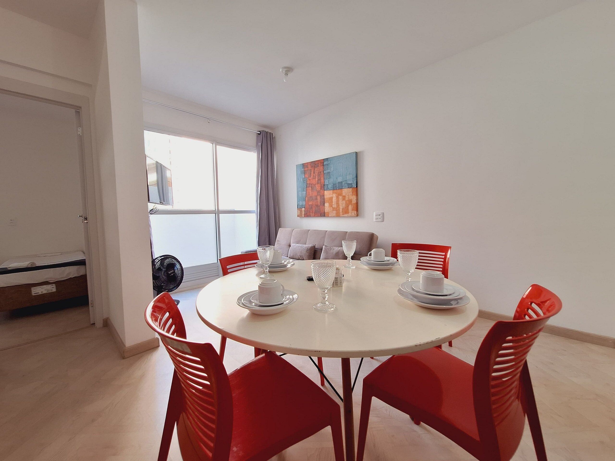 A dining area with a round table, red chairs, and a view of the outside through a large window.