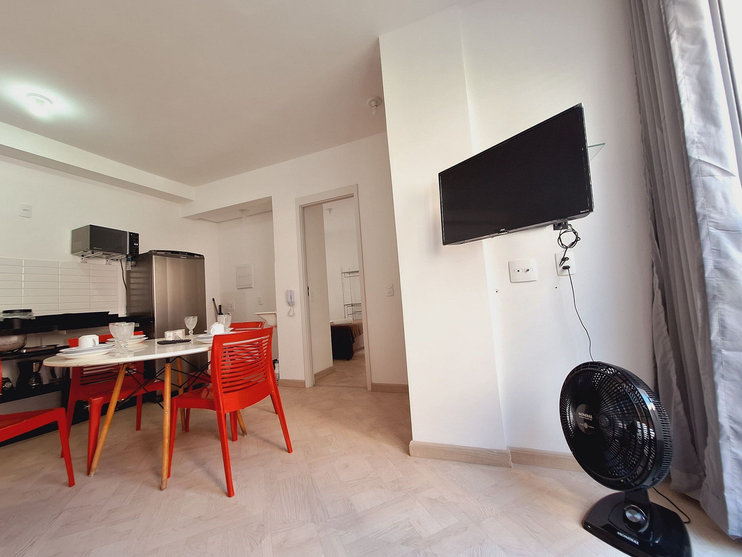 A modern kitchen with a dining area, a flat-screen TV mounted on the wall, and a standing fan.