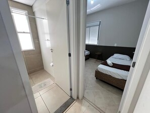 Ein Schlafzimmer mit Bett, Nachttisch, Fenster und einer Tür zu einem anderen Raum.
