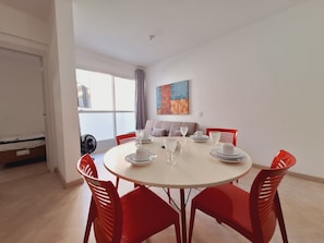 Un comedor con una mesa redonda, sillas rojas y vistas al exterior a través de un amplio ventanal.
