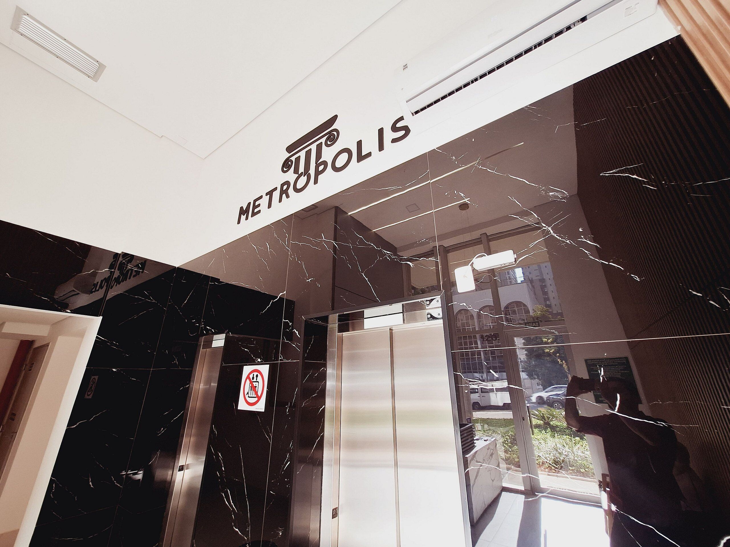Entrada de um prédio com uma placa indicando 'METROPOLIS' e um aviso de proibido fumar.