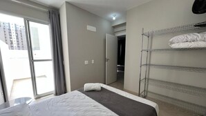 A hotel room with a bed, a window with curtains, a door, and a metal shelf unit. - LK Centro 2 (Belo Horizonte)