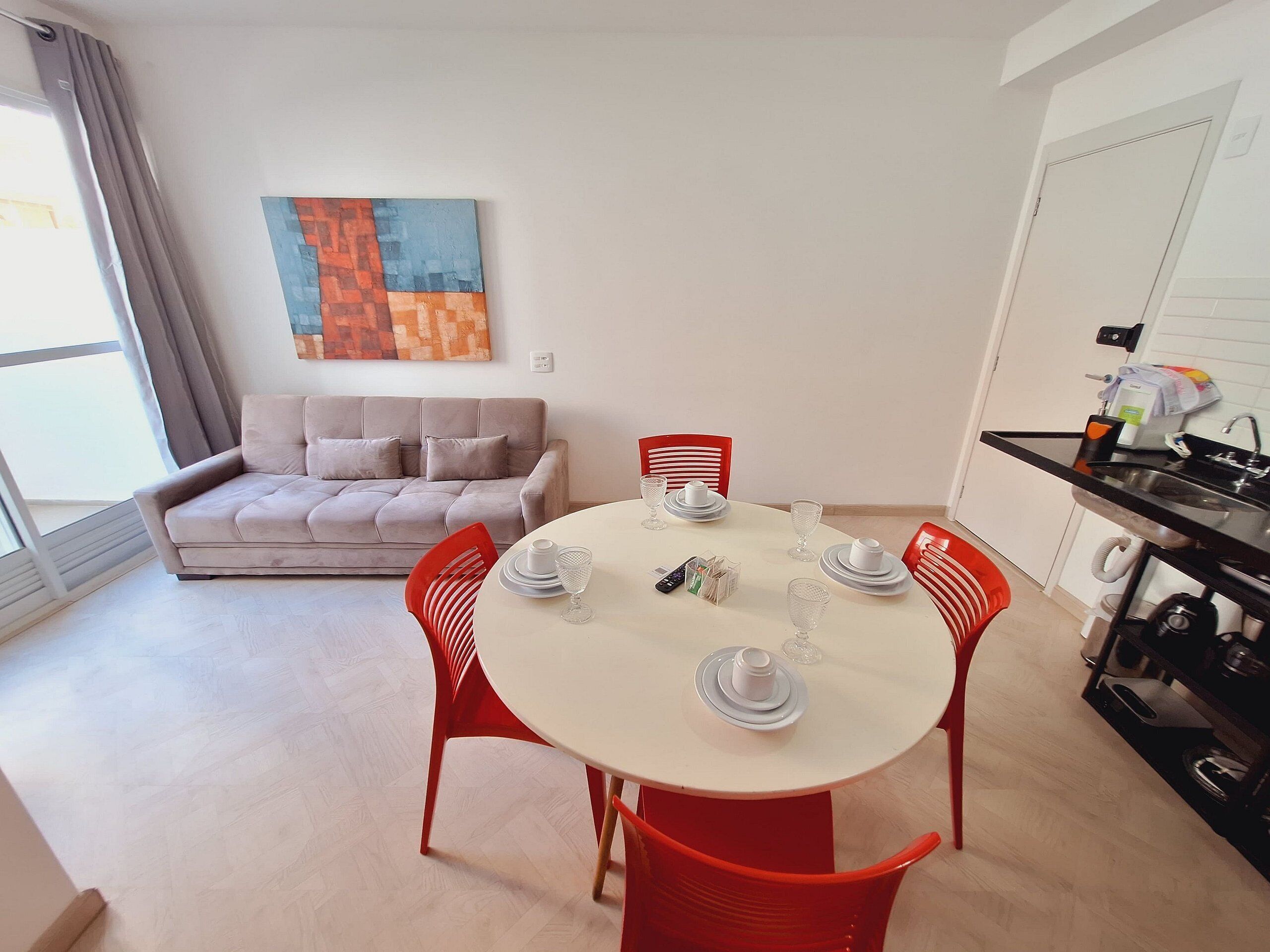 Uma sala de estar moderna com um sofá, uma mesa de jantar posta com pratos e copos, e uma área de cozinha com pia e armários.