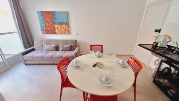 Uma sala de estar moderna com um sofá, uma mesa de jantar posta com pratos e copos, e uma área de cozinha com pia e armários.