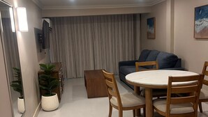 A modern living room with a round dining table, wooden chairs, a sofa, and a TV mounted on the wall. - Paria Suites Hotel and Conference Center (La Romain)