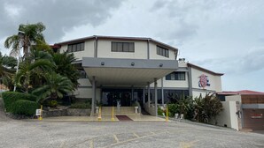 A multi-story building with a covered entrance, palm trees, and a sign for 'The Lodge Bar & Lounge'. - Paria Suites Hotel and Conference Center (La Romain)