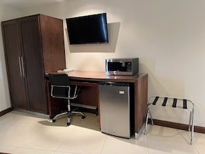 A compact office space with a wooden desk, a black chair, a microwave, a dishwasher, and a TV mounted on the wall.