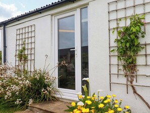 Ein Haus mit weißer Fassade, einer Schiebetür und einem Holzrankenwerk mit Kletterpflanzen.