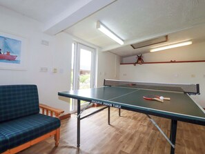 Una habitación con mesa de ping pong, sofá, un cuadro y una ventana.