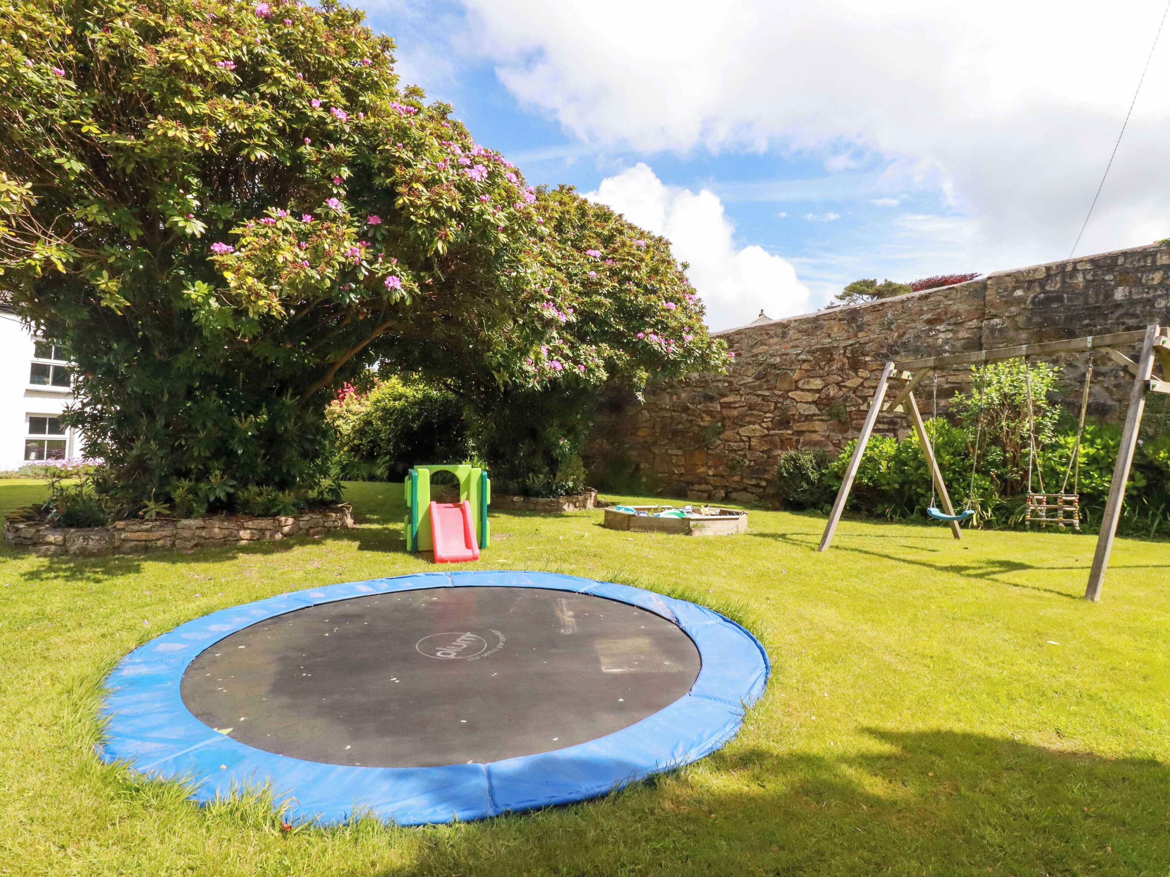 Patio trasero con un trampolín, un tobogán y un columpio.