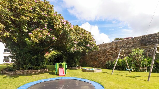 Ein Garten mit Trampolin, Rutsche und Schaukel.
