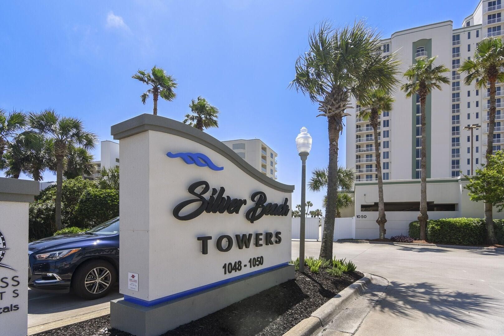 A sign for Silver Beach Towers with a clear sky and palm trees.